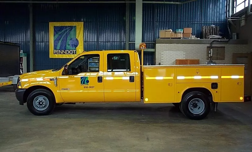 An image showing a side view of a yellow PennDOT crew cab pickup truck parked in a garage.